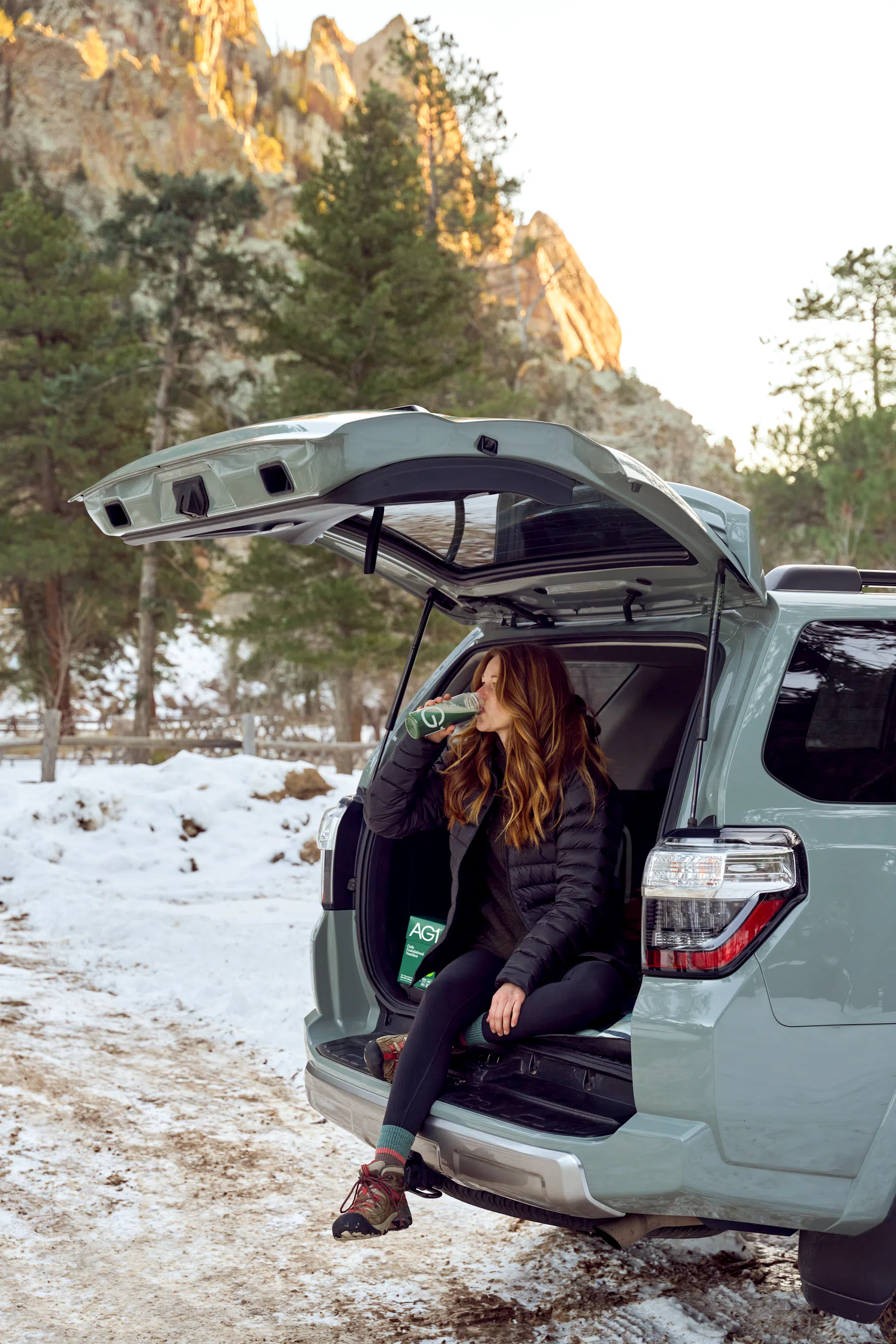 Een vrouw neemt een slok van een drankje met AG1 en zit in een kofferbak van een auto